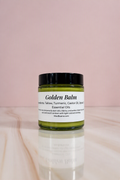 Moo Bueno Skincare Golden Balm, 4 oz glass jar of turmeric tallow body balm on a pink backdrop